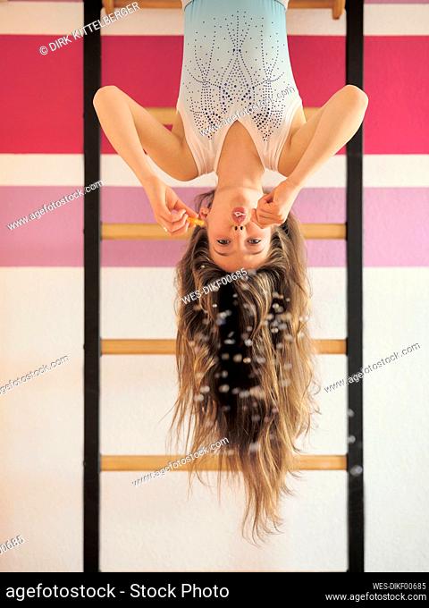 Girl blowing bubbles hanging upside down on wall bars