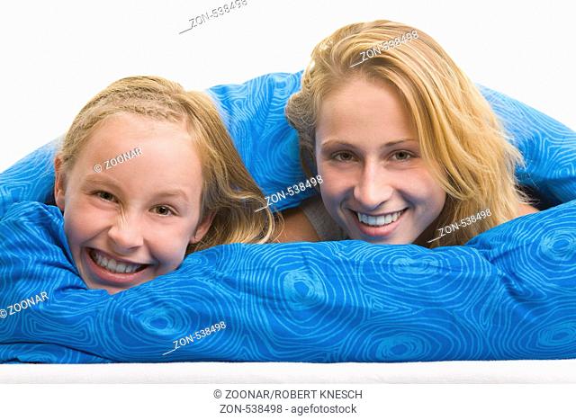Blondes Mädchen liegt mit ihrer Mutter lachend unter einer Bettdecke