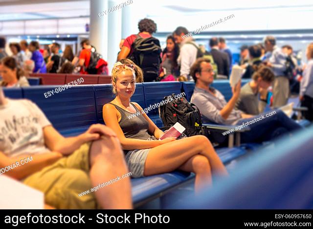 Casual blond young woman waiting to board a plane at airport departure gates, holding flight ticket and passport in her hands