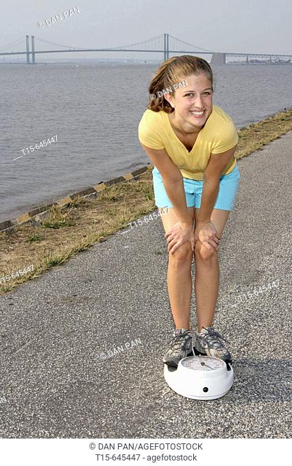 Woman in her 20's looking happy and smiling on the scale after working out by the river