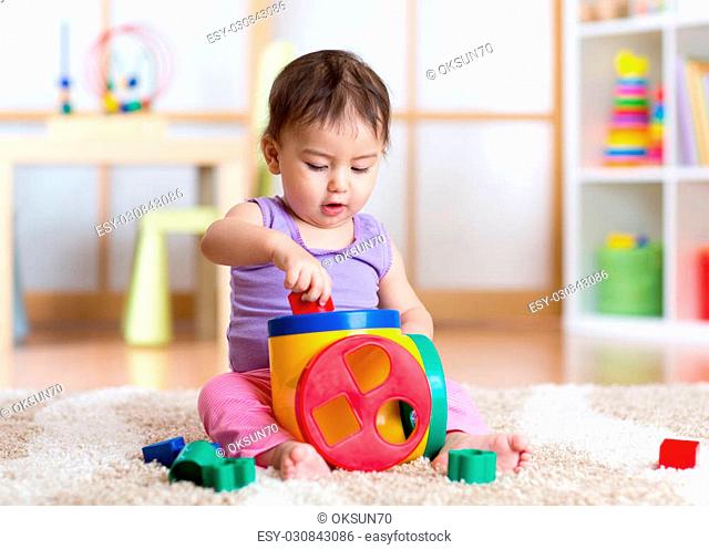 Cute toddler girl playing indoors with sorter toy sitting on soft carpet