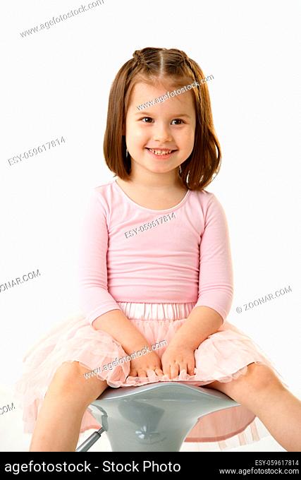 Portrait of happy little girl wearing ballet costume sitting on high chair against white background, smiling
