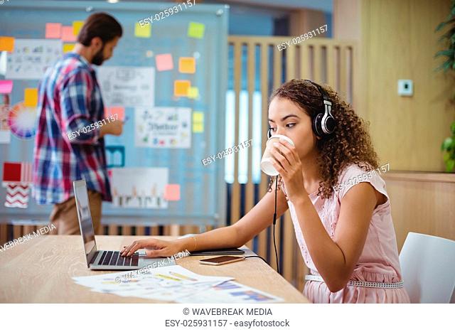 Female graphic designer drinking coffee while using laptop