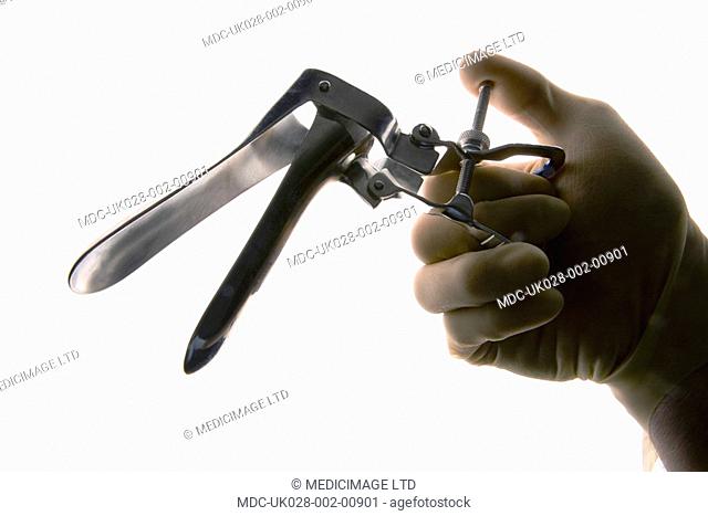 Gloved hand holding a vaginal speculum. The vaginal speculum is used as a medical tool to hold open the vagina during medical investigation