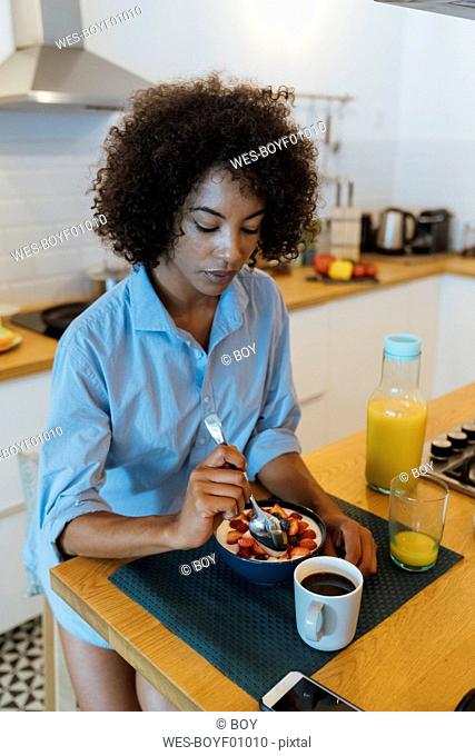 Woman having breakfast in her kitchen, eating fruit