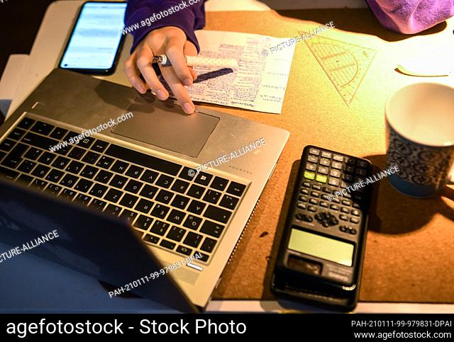 08 January 2021, Berlin: A girl is sitting at her desk at home doing assignments for school. For this she writes on her laptop and paper