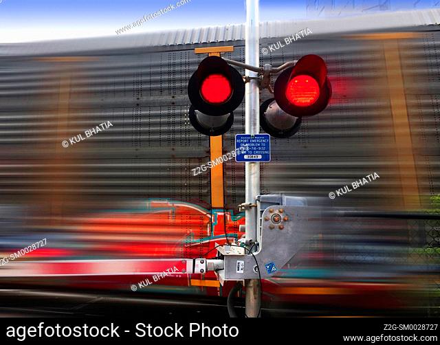 A train speeds past a railway crossing barrier, red lights flickering, Ontario, Canada