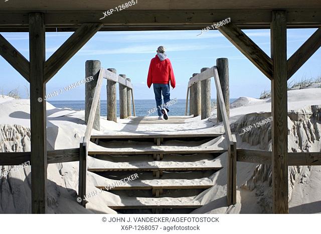 Woman walking on to a beach through a boardwalk shelter  Lavalette, New Jersey, USA