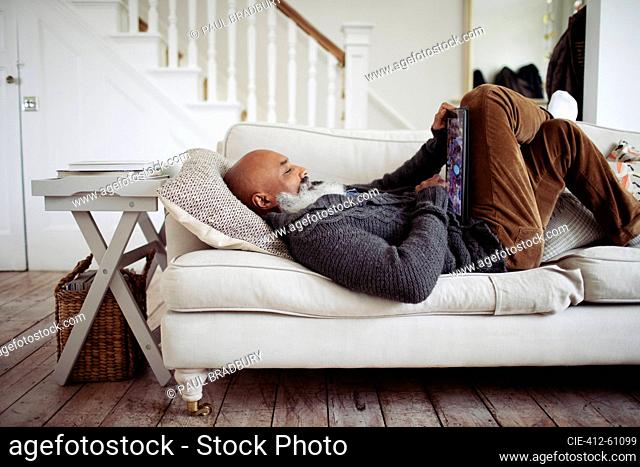 Mature man relaxing on living room sofa with digital tablet