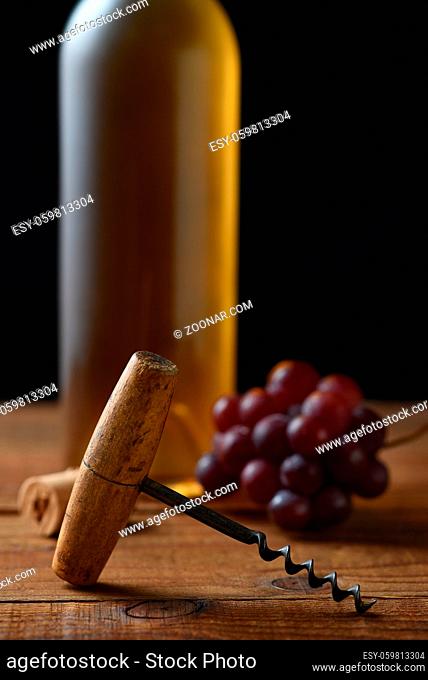Wine Still Life: Closeup of an antique cork screw with out of focus white wine bottle grapes and cork in the background