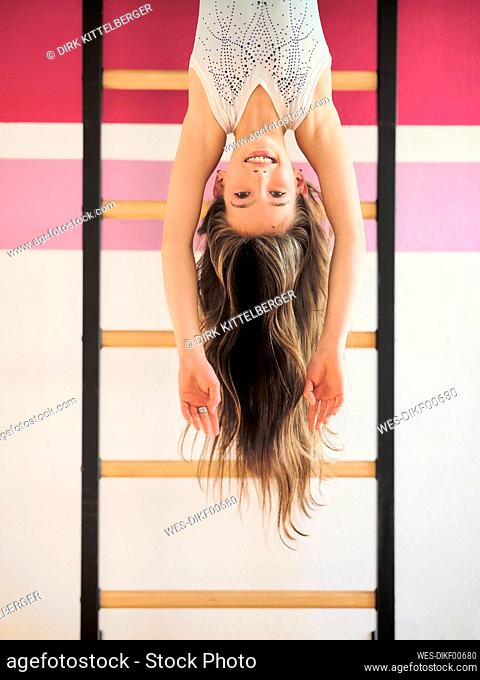 Smiling girl hanging upside down on wall bars