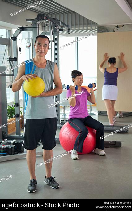 Mature man holding ball in the gym, people exercising on the background