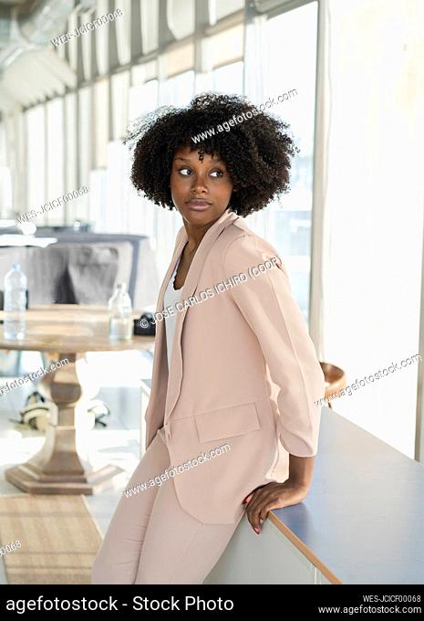 Businesswoman with curly hair leaning on table at office