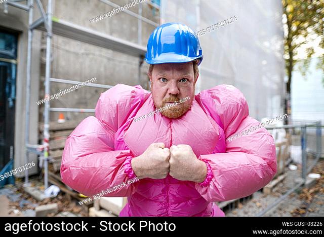 Portrait of man wearing pink bodybuilder costume and hard hat at construction site