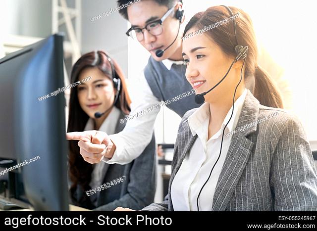Young adult confidence with smiling supervisor teaching to his team of operator team agent with headsets and desktop computer in a call center to monitor her...