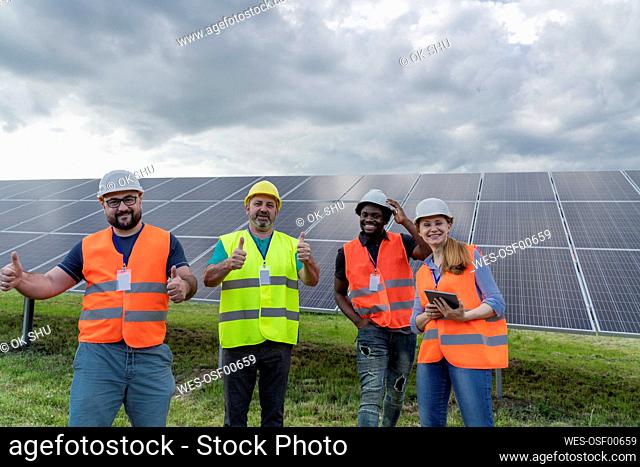 Happy engineers showing thumbs up gesture standing at solar power station