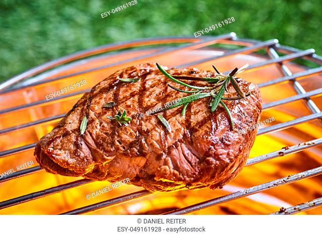 Thick juicy portion of beef fillet steak garnished with fresh rosemary on the BBQ grilling over the glowing hot coals in a close up view outdoors