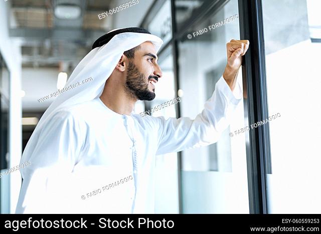 handsome man with dish dasha working in his business office of Dubai. Portraits of a successful businessman in traditional emirates white dress