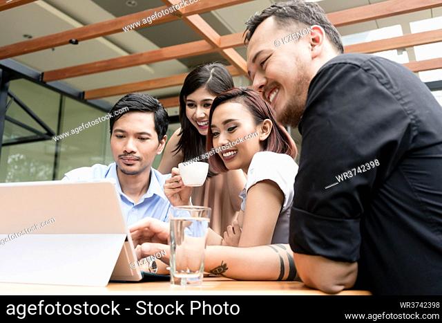 Group of four young Asian people having fun while sitting together outdoors at a coffee shop with wireless internet connection