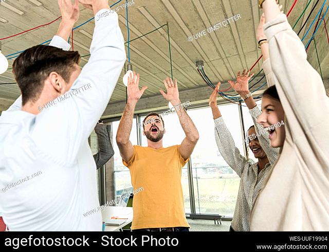 Happy young business people raising their arms in office
