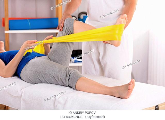 Physiotherapist Giving Leg Treatment To Woman With Yellow Exercise Band
