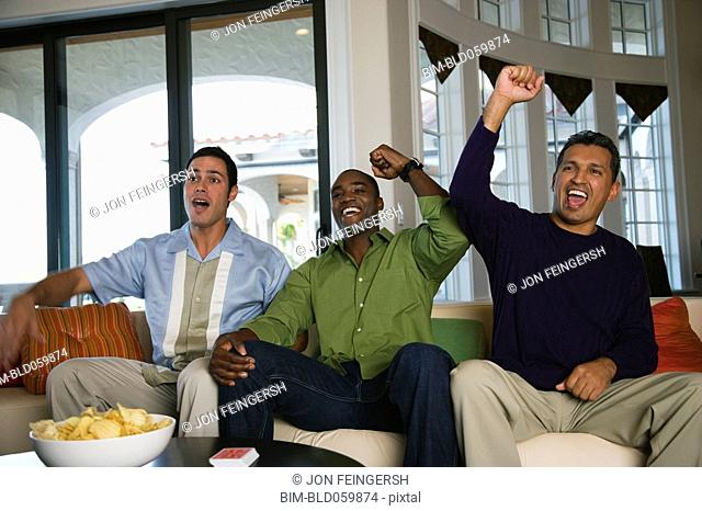 Multi-ethnic men cheering on sofa