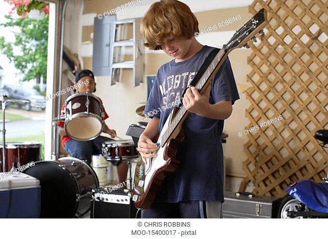Two boys 10-12 playing drums and guitar in garage