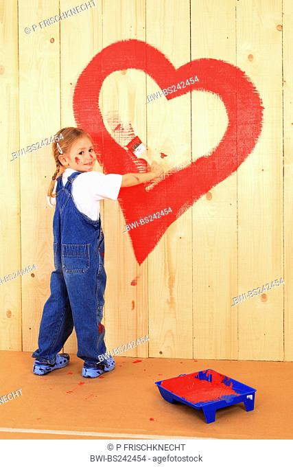 smiling little girl painting a heart onto a wooden wall with red paint