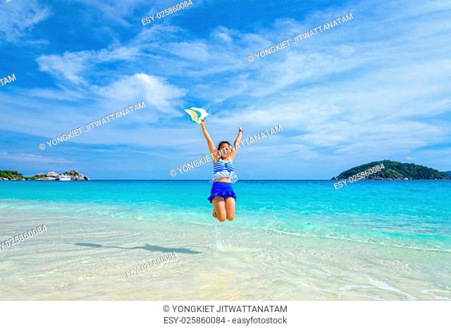 Tourist girl in a blue white striped swimsuit jumping with happy on the beautiful beach and sea during summer at Koh Miang Island, Mu Ko Similan National Park
