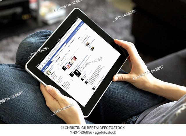 Close up view of a woman handholding an ipad reading her Facebook newsfeed in a livingroom