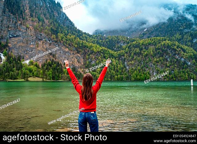 Beautiful young girl is raising his hands up against the backdrop of magnificent mountain lake