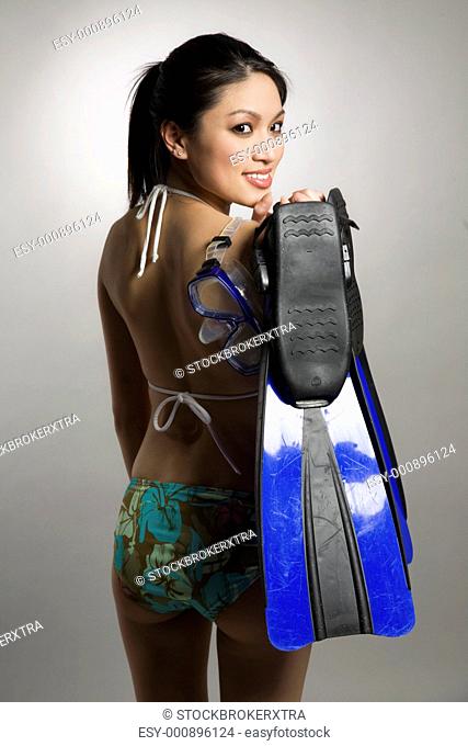 A shot of a beautiful asian woman wearing bikini and carrying snorkelling equipment