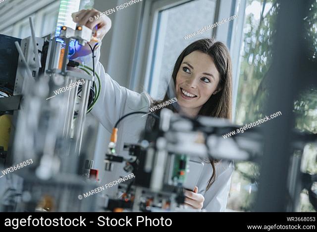 Smiling young woman inventing machinery in laboratory