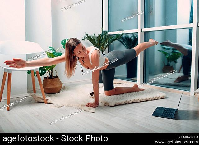 Adult woman doing yoga at home living room with online tutorials on laptop