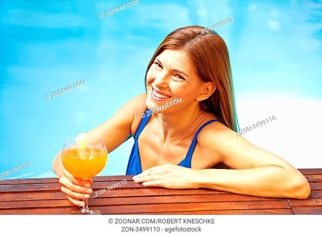 Attraktive lachende ältere Frau mit einem Cocktail im Pool