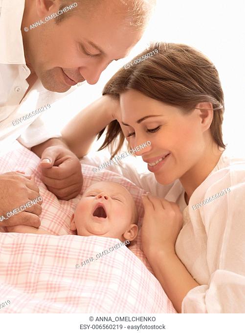 Newborn baby awake, parents looking on child, loving family, mother and father with little daughter on the bed at home, love concept
