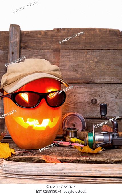 halloween pumpkin head in hat with fishing tackles on wooden boards background