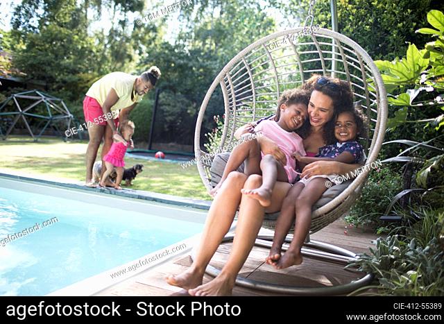 Happy mother and daughters cuddling in summer patio swing chair
