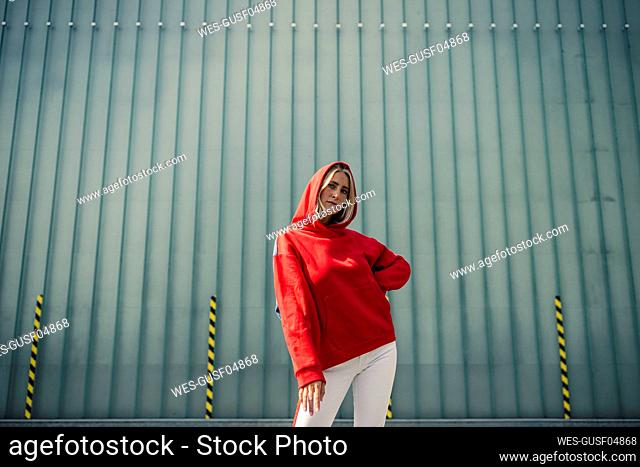 Carefree woman with hand raised standing on footpath against wall