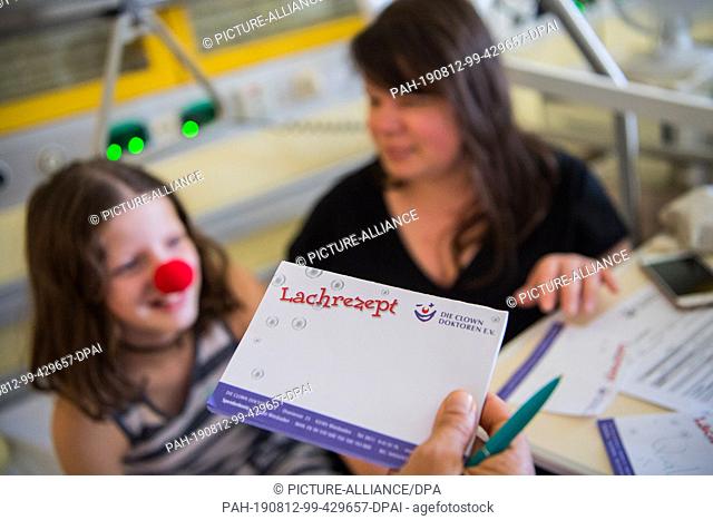 27 June 2019, Hessen, Wiesbaden: Consent was given in writing by the parents. Emma (I) gets a laugh prescription from the clown doctor