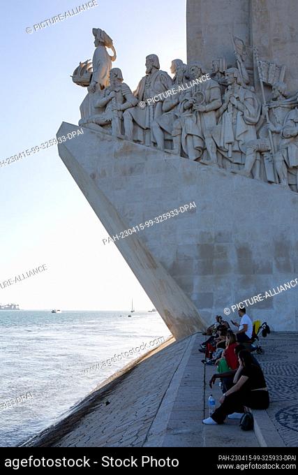 PRODUCTION - 06 April 2023, Portugal, Lissabon: Day trippers sit near the Monument to the Discoveries in Lisbon's Belem district on the banks of the Tagus River