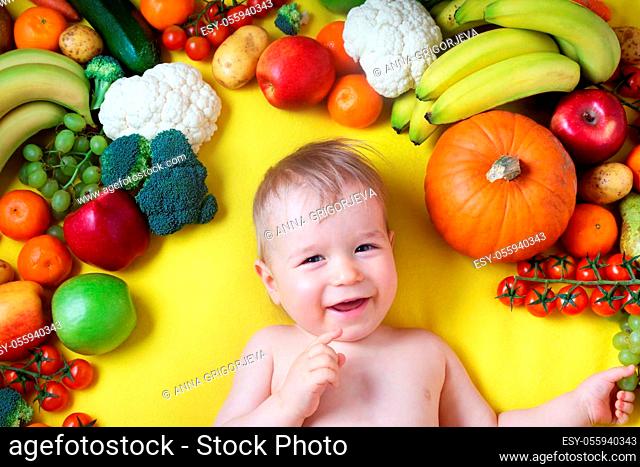 baby surrounded with fruits and vegetables on yellow blanket, healthy child nutrition