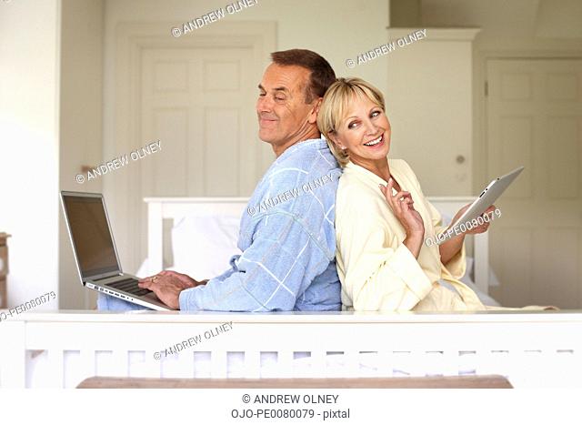 Couple in bedroom using laptop and digital tablet