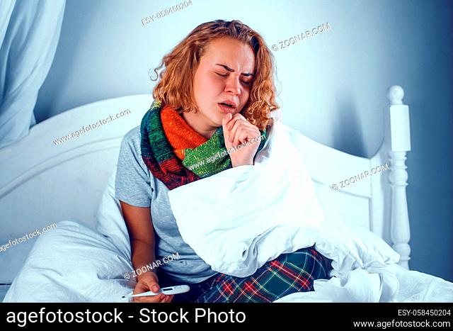 Sick girl is coloured wool scarf sits in bed and coughs. Ill woman in bed coughing