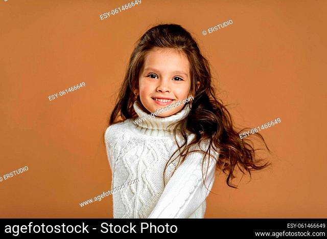 Cute smiling little child girl in white sweater looking to camera on beige background. child with flying hair