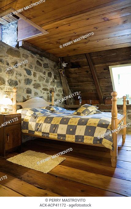 Double bed and furnishings in a guest room on the upstairs floor of an Old Canadiana 1722 cottage style fieldstone and wooden siding Residential Home, Quebec