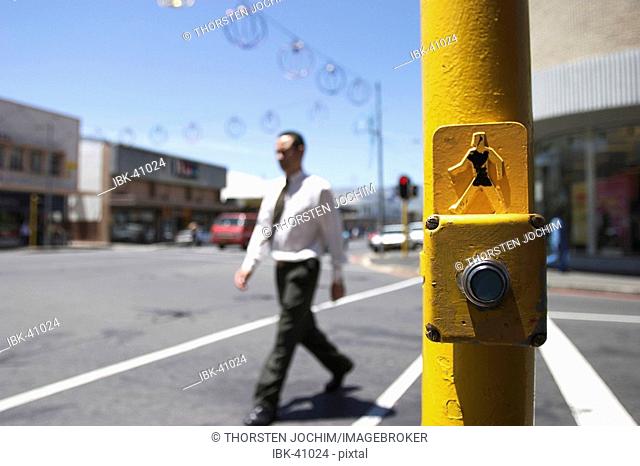 Crosswalk with yellow car-stop button and a businessman crossing. (Paarl - South-Africa)