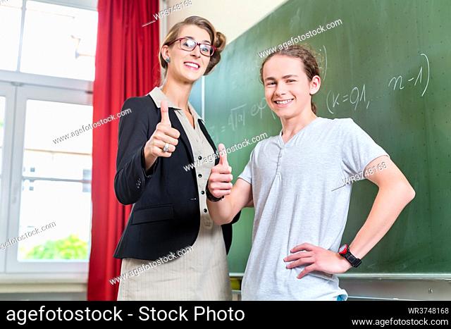 School class Teacher and student stand in front of a blackboard with math work in a classroom during lesson