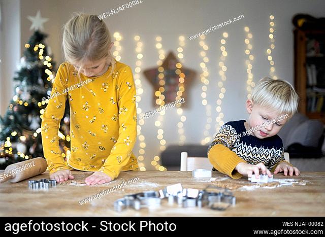 Siblings preparing cookies at table on Christmas
