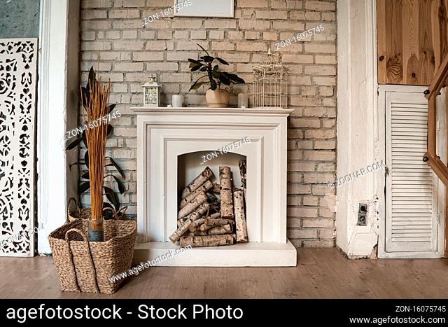 White fireplace in a brick wall. There's wood in the fireplace. Nearby wicker basket with decorative dry plants. High quality photo